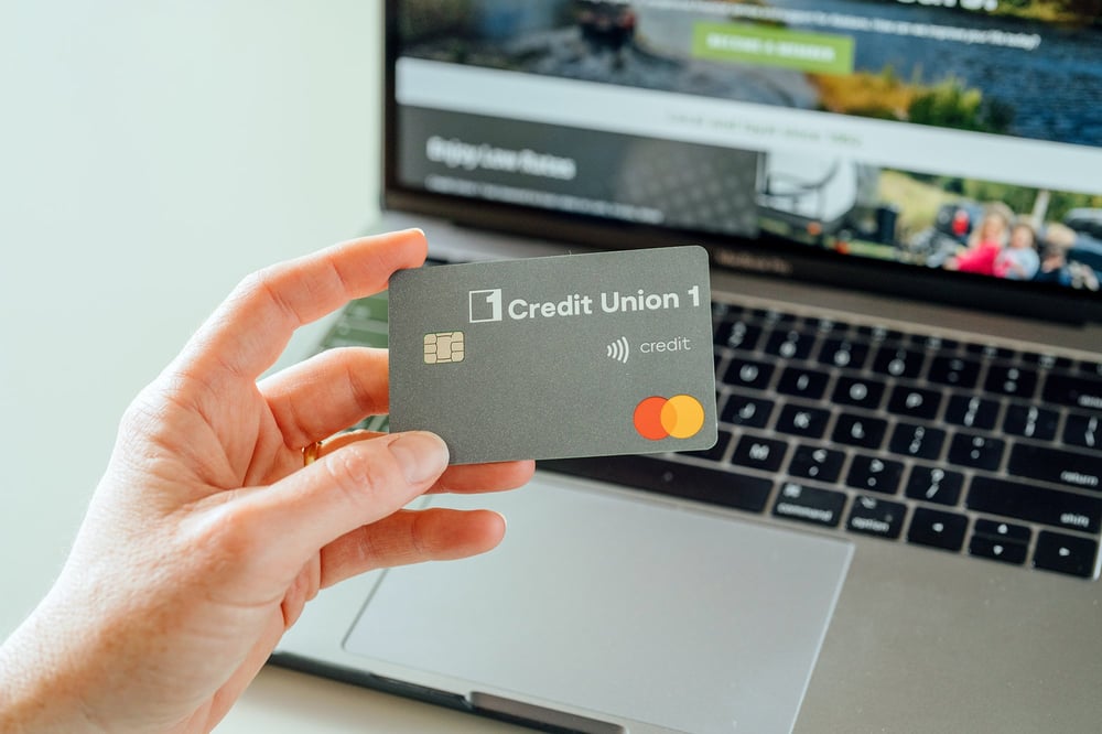 Person holding their CU1 credit card in front of the their computer with the cu1.org website displayed in the background