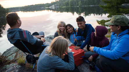 Group of people around an Alaskan lake, eating out of a picnic basket