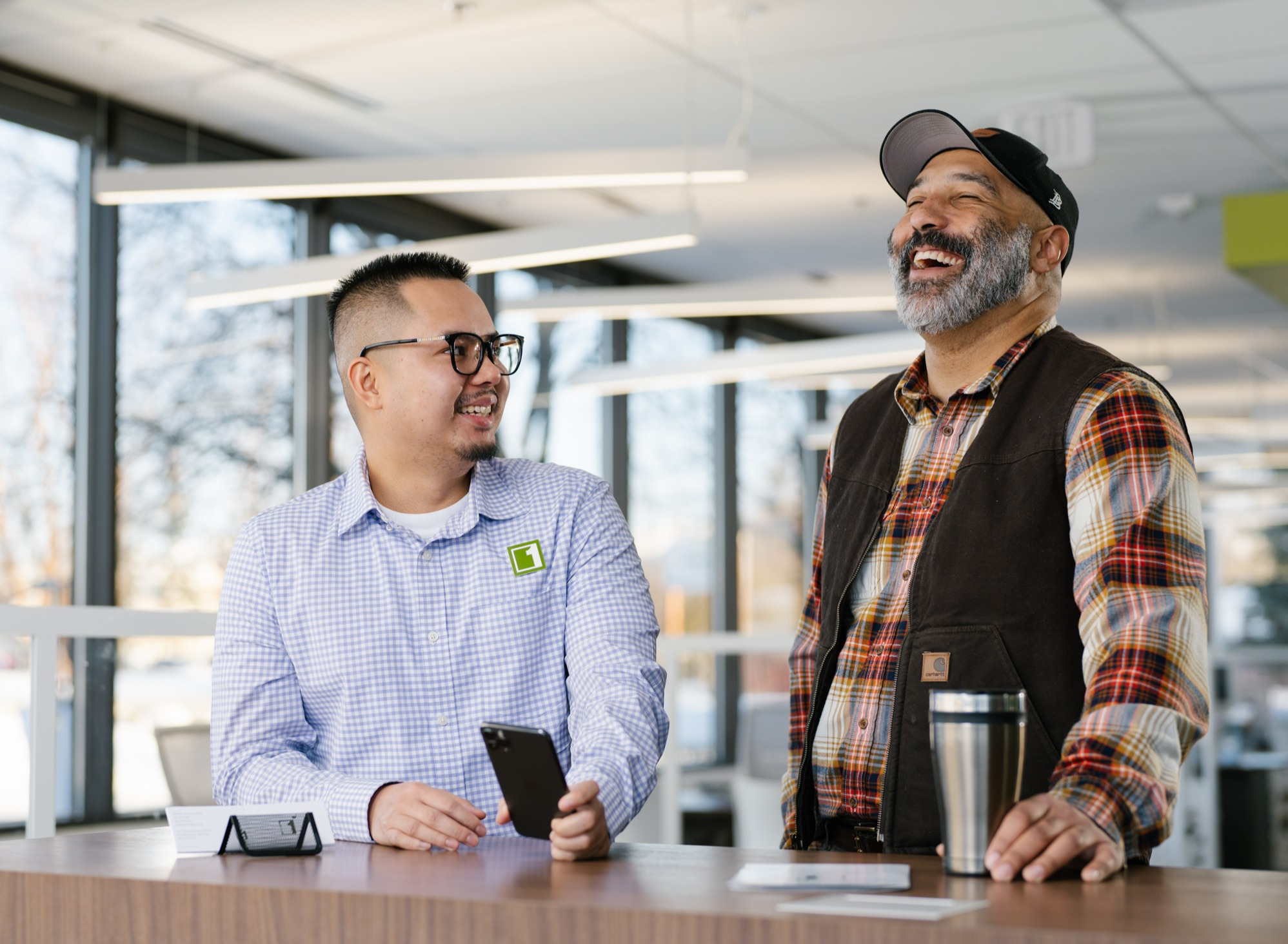 Two people laughing with each other, one man is holding a phone