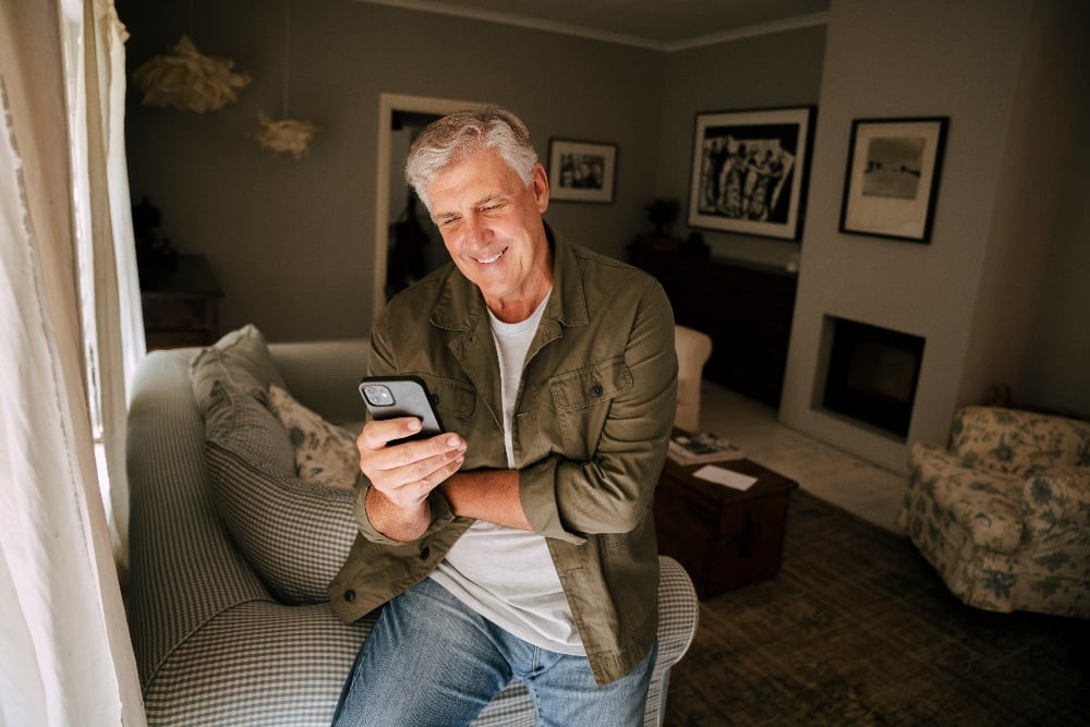 Older man sitting on his couch looking at his phone