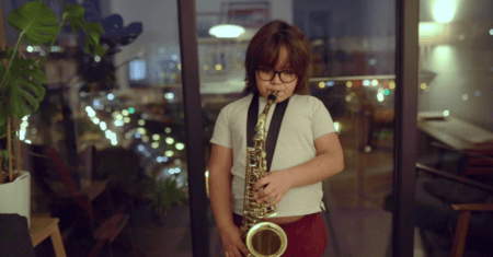 Young boy blowing on a saxophone in a room full of windows