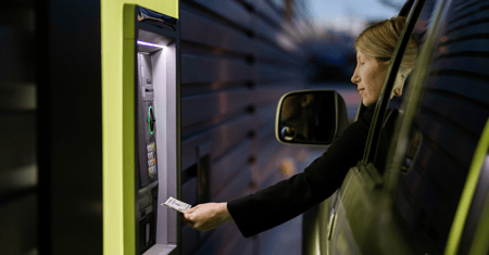 Woman reaching out of her car to add a debit card into an interactive teller machine.