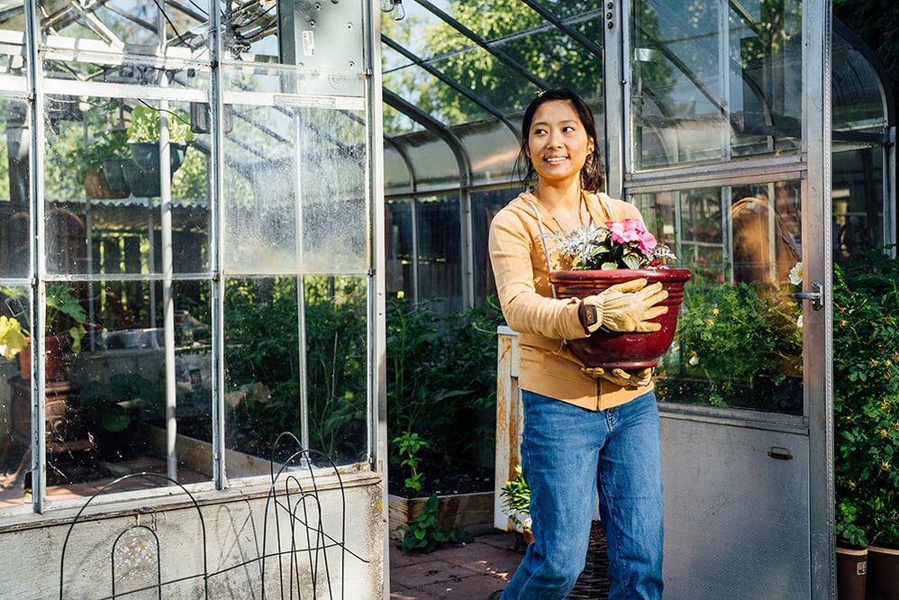 Woman walking out of green house carrying a pot of summer plants