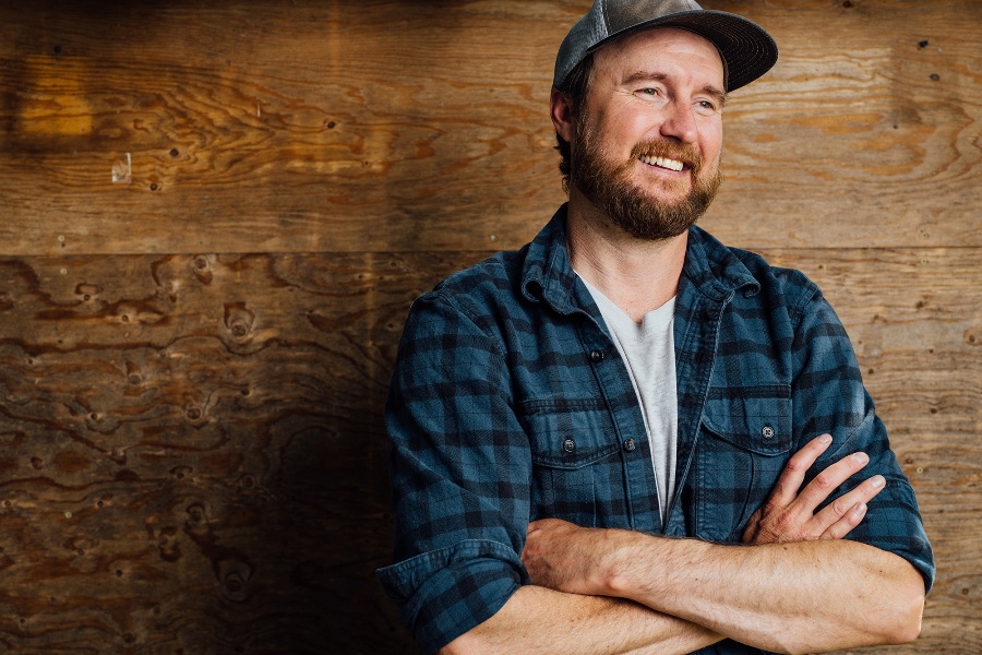 Man standing against wood wall, arms crossed and looking off to the right smiling